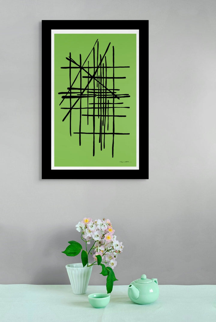 Framed abstract art in green displayed on a wall above a table with decorative vase.