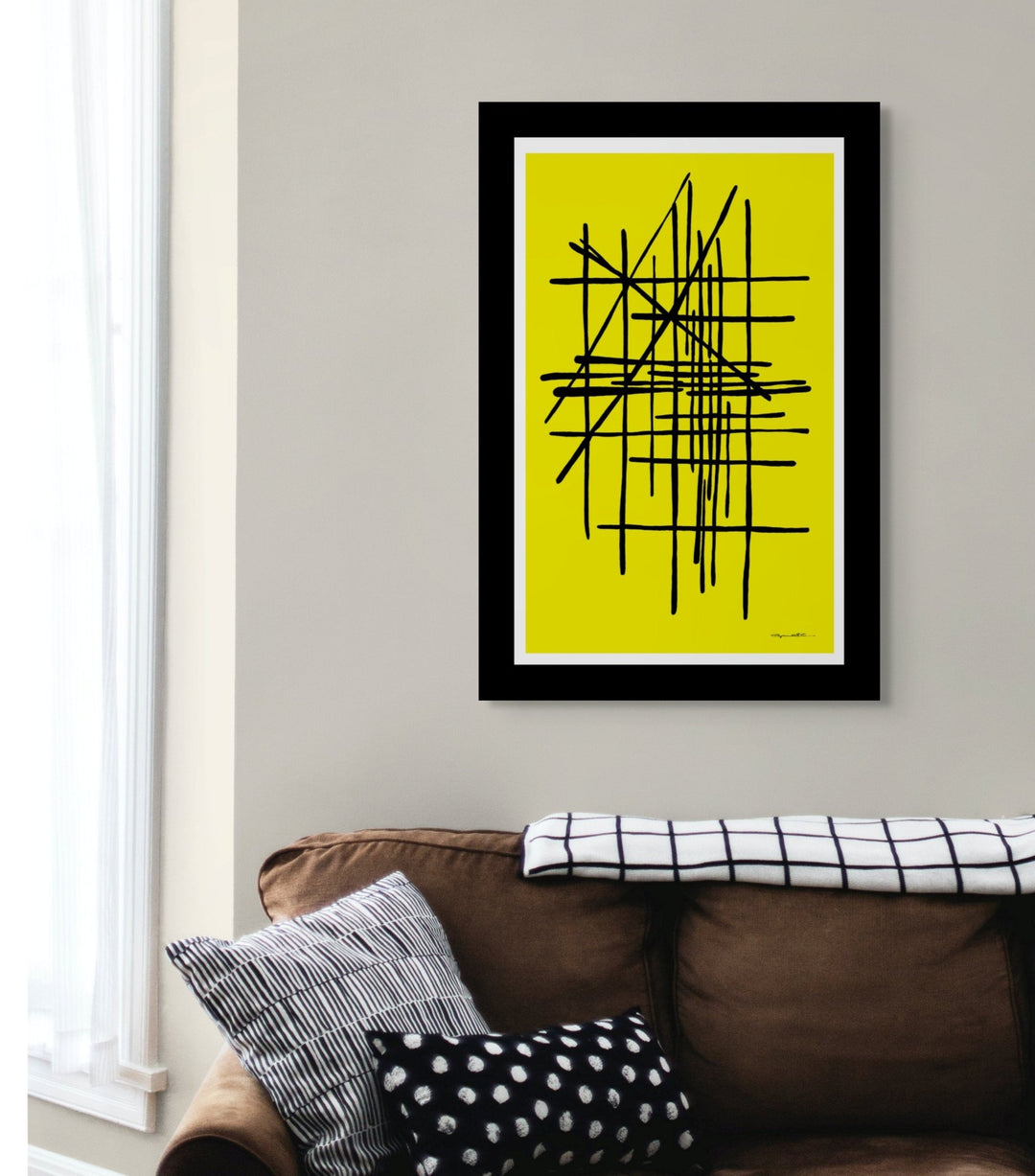 Framed abstract art with black lines on a yellow background, hanging above a brown sofa with patterned cushions.