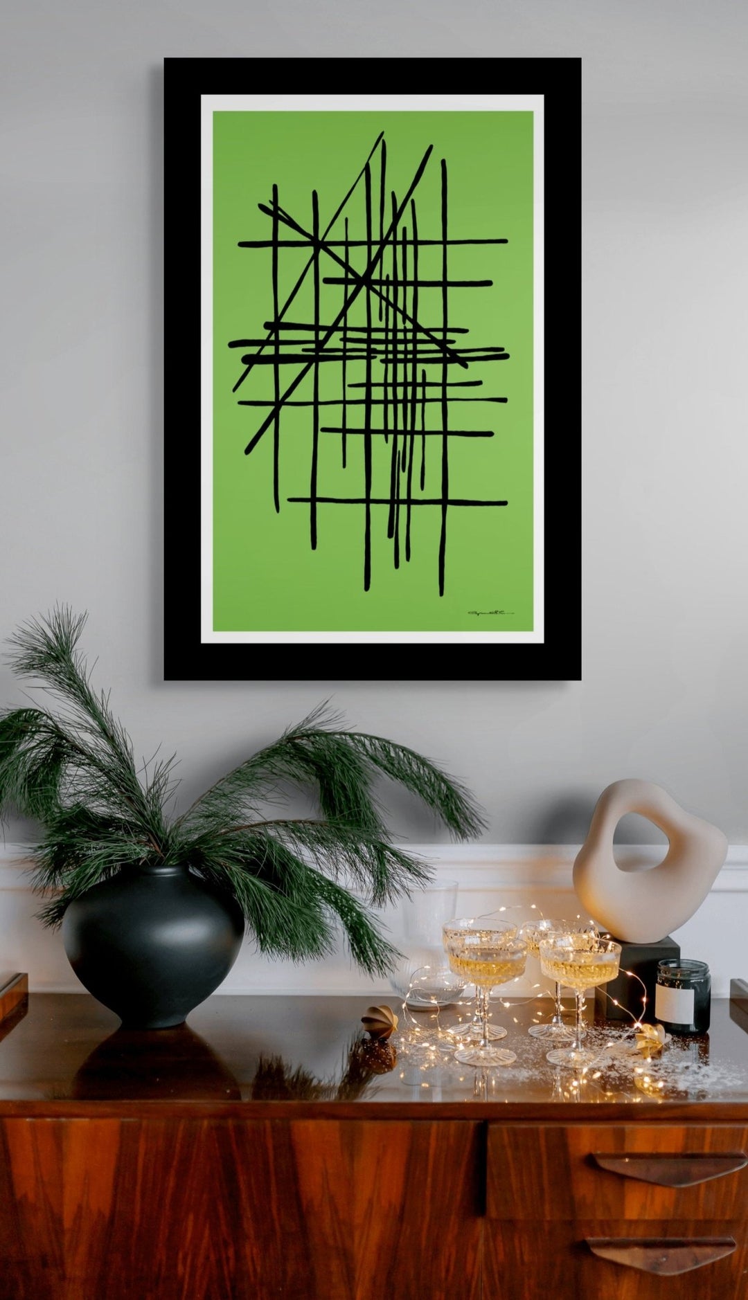 Framed abstract artwork in green displayed in a room with decor elements.
