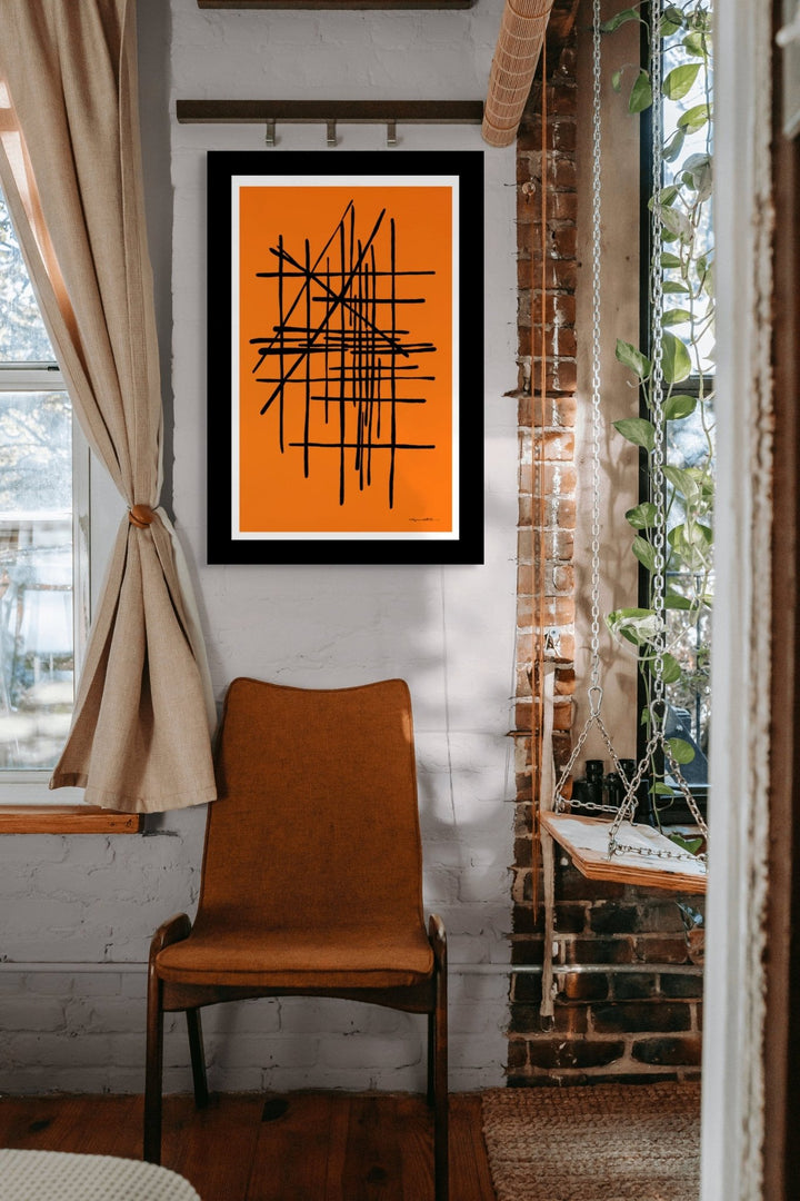 Framed abstract artwork on an orange background in a room with a brick wall and window.