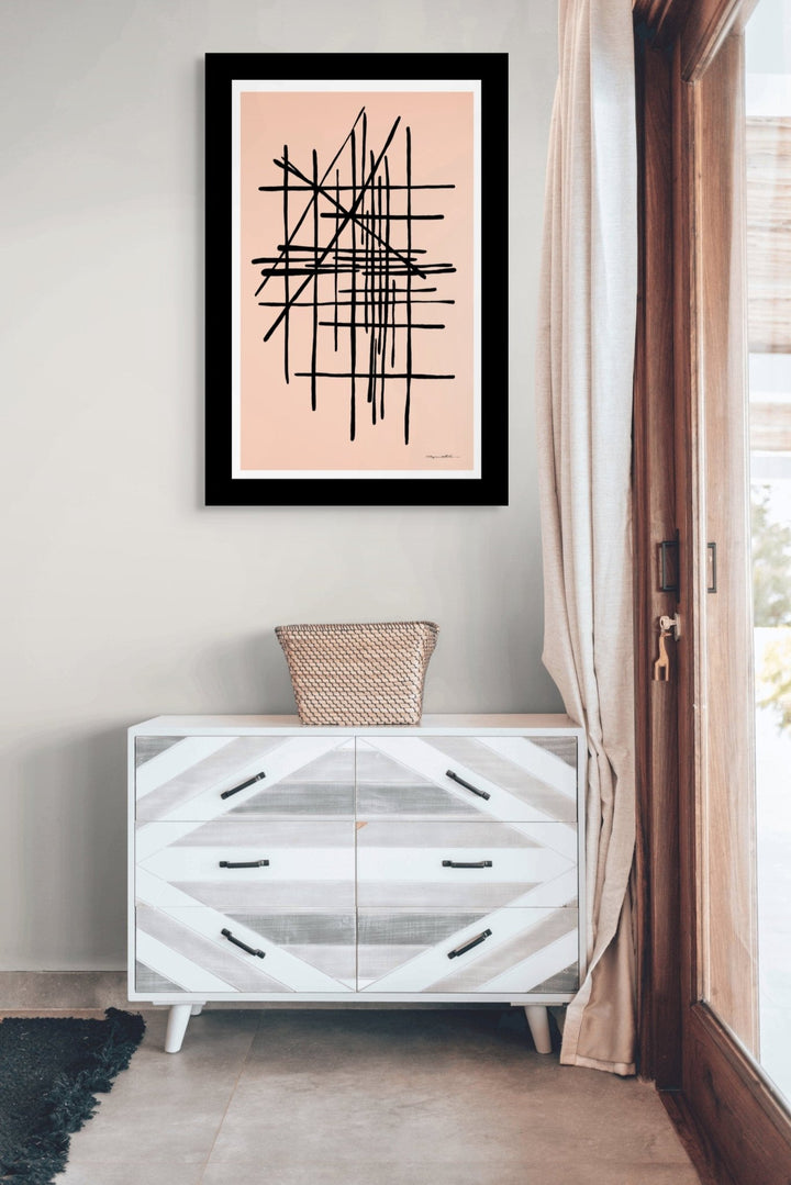 Framed pink abstract art on a wall above a white dresser with geometric design.