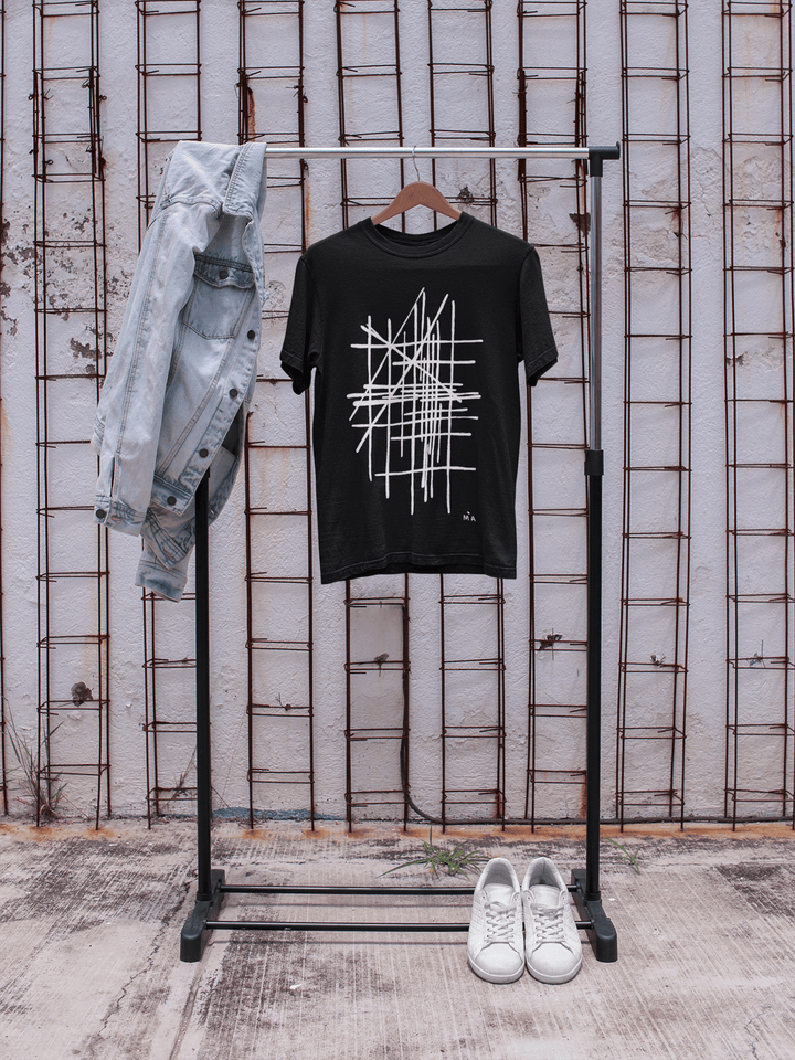 Black abstract t-shirt with white geometric design on a rack against a textured wall.