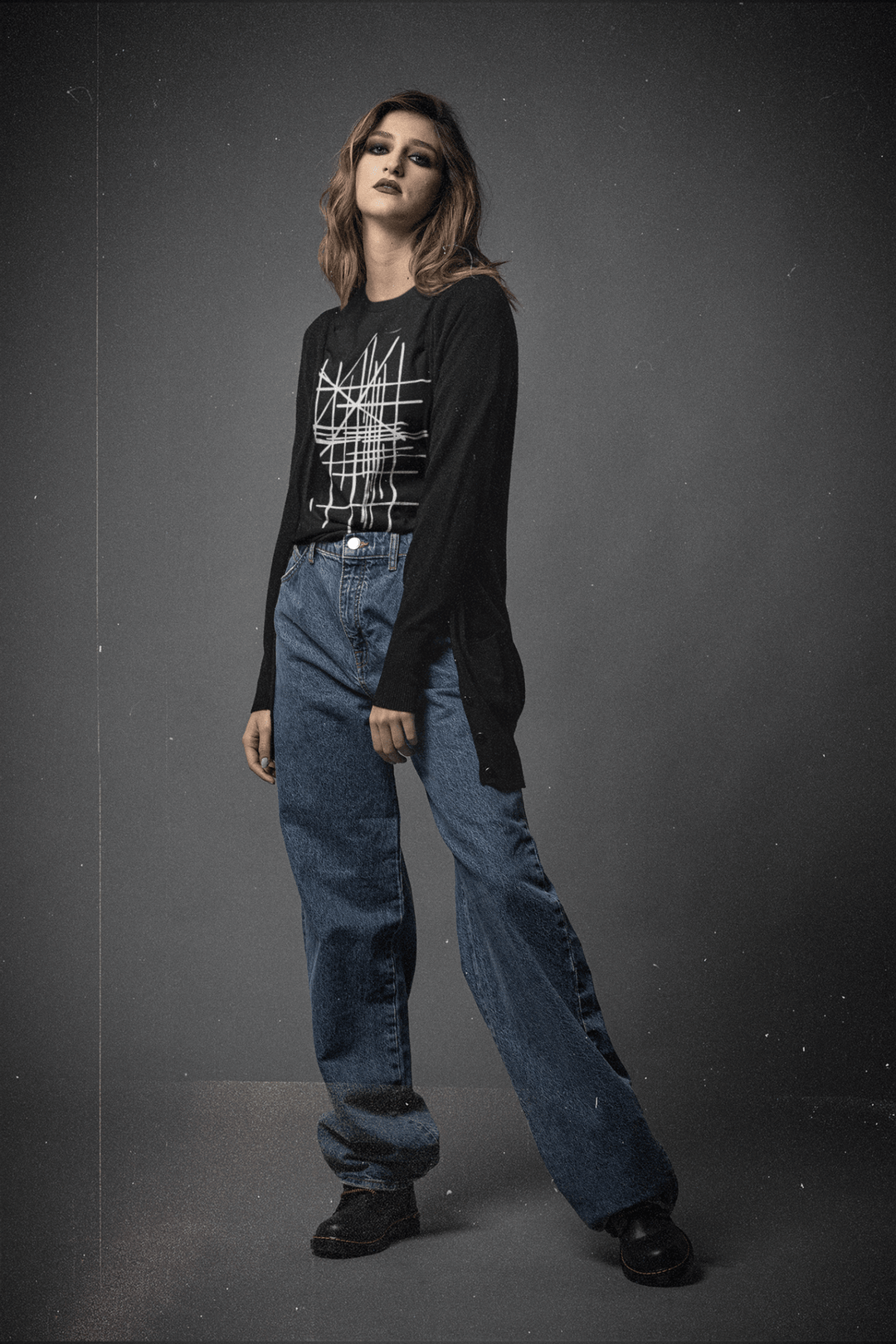 Woman wearing a black sweater with a geometric design and blue jeans on a gray background