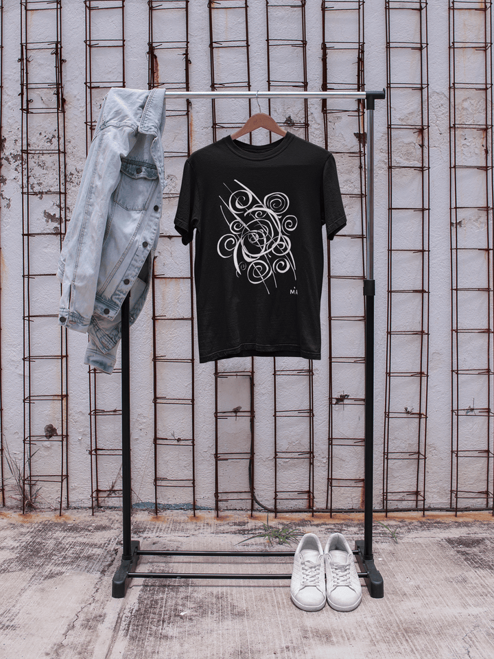 The Trend - Abstract T-Shirt by Miamiabstract.com, featuring a black silk fabric with a white swirl design, hangs next to a light blue denim jacket, while white sneakers rest below by a wall with exposed metal rods.