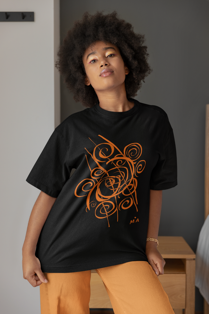 A woman with curly hair stands confidently indoors by a nightstand and bed, wearing the Trend - Abstract T-Shirt by Miamiabstract.com, featuring an orange graphic design, paired with matching orange pants.